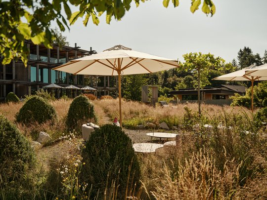 BERGEBLICK: Ihr Hotel in Bad Tölz Sonnenschirme und Sitzgelegenheiten in einem Garten mit hohem Gras und Büschen