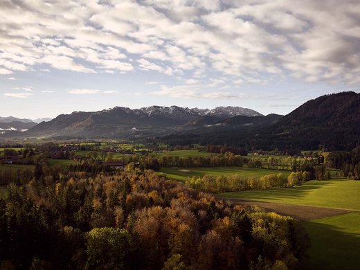 Dein Aktivurlaub in Bayern in Bad Tölz Herbstliche Landschaft mit farbigen Bäumen, grünen Feldern und Bergen im Hintergrund