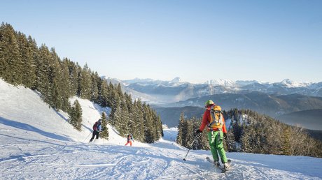 Aussicht auf Traumurlaub in Bad Tölz Skifahrer fahren auf schneebedeckter Piste mit Bergen und Tannen im Hintergrund