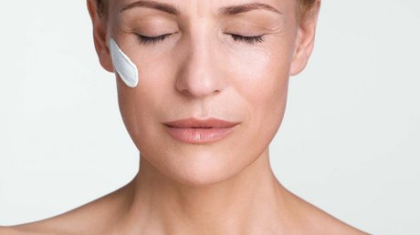 Aussicht auf Traumurlaub in Bad Tölz Frau mit geschlossenen Augen, trägt Gesichtscreme auf der Wange, betet mit gefalteten Händen