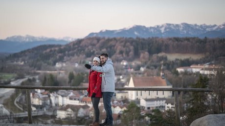 Aussicht auf Traumurlaub in Bad Tölz Paar macht Selfie mit Bergkulisse und Stadt im Hintergrund