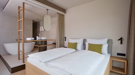 Aussicht auf Traumurlaub in Bad Tölz Modernes Hotelzimmer mit Doppelbett und offenen Badezimmer mit Badewanne