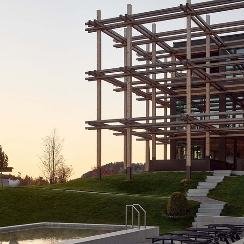 Hotel BERGEBLICK in Bavaria Modern terrace with lounge chairs, pool, and wooden frame structure at sunset