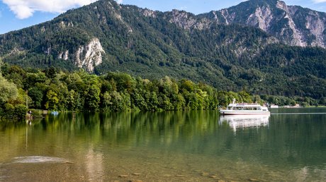 Aussicht auf Traumurlaub in Bad Tölz Fähre auf klarem See vor bewaldeten Bergen unter blauem Himmel