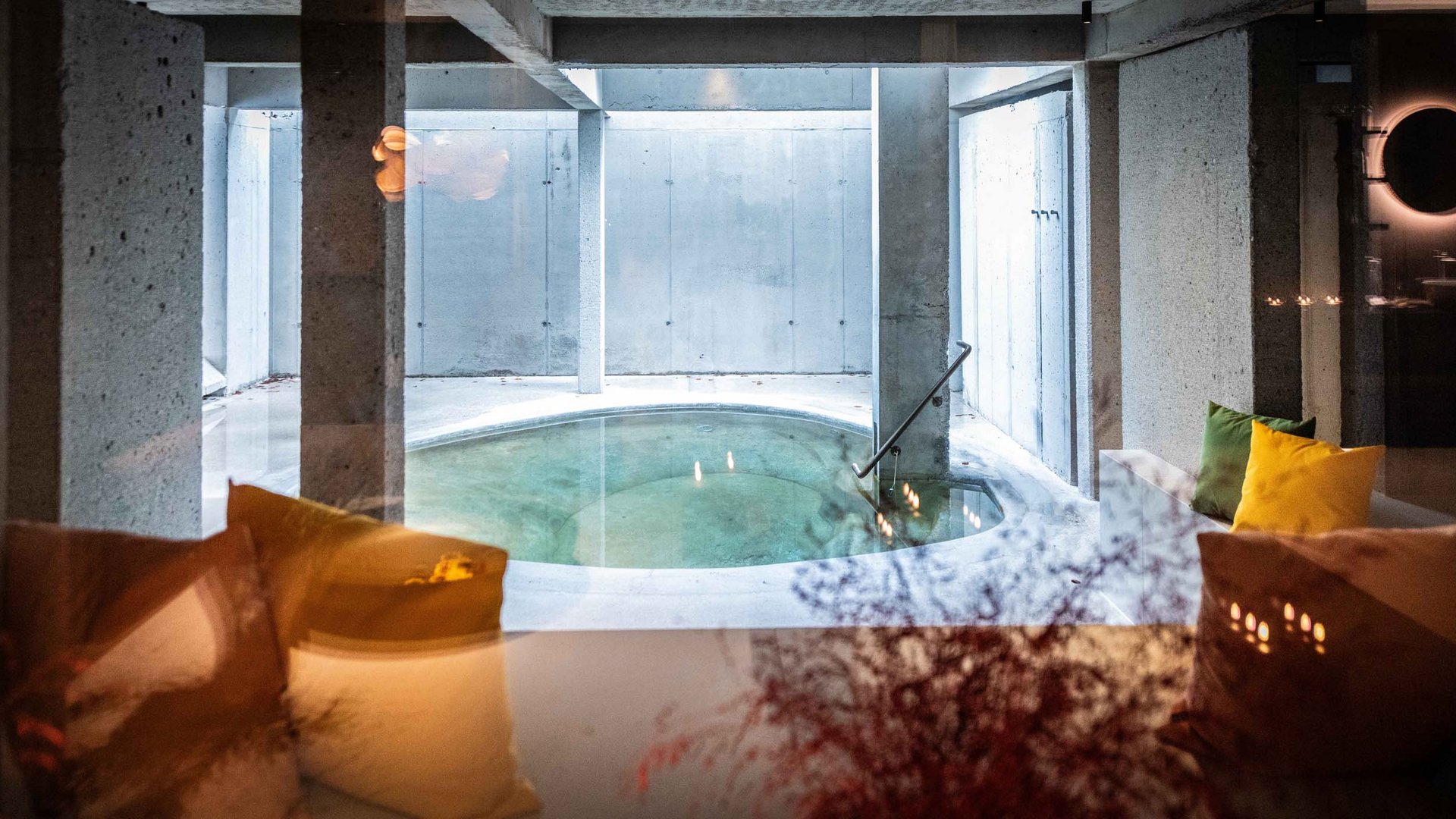 BERGEBLICK: Ihr Hotel in Bad Tölz Runder Innenpool mit Betonwänden und bunten Kissen auf Sofas im Vordergrund