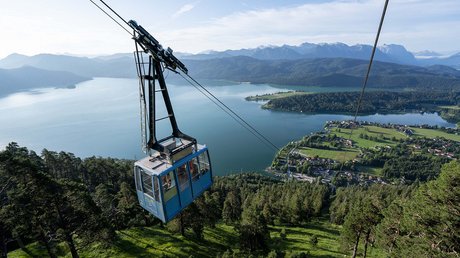 Aussicht auf Traumurlaub in Bad Tölz Blaue Seilbahn über grünem Wald mit Blick auf See und Berge