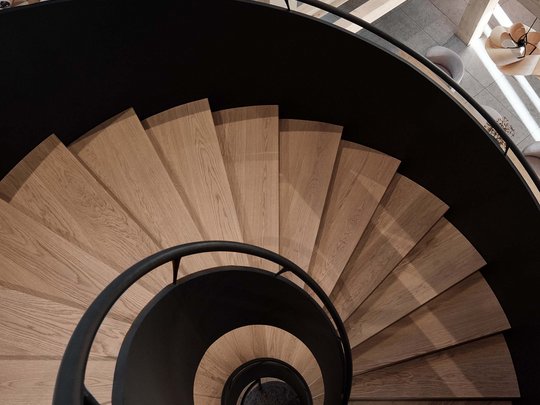 BERGEBLICK: Ihr Hotel in Bad Tölz Spiralförmige Holztreppe mit schwarzem Geländer in modernem Innenraum