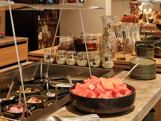 BERGEBLICK: Ihr Hotel in Bad Tölz Frühstücksbuffet mit Müsli, Wassermelone und verschiedenen Zutaten in Gläsern
