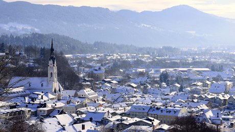 Aussicht auf Traumurlaub in Bad Tölz Verschneite Stadt mit Kirche vor bewaldeten Bergen im Winter