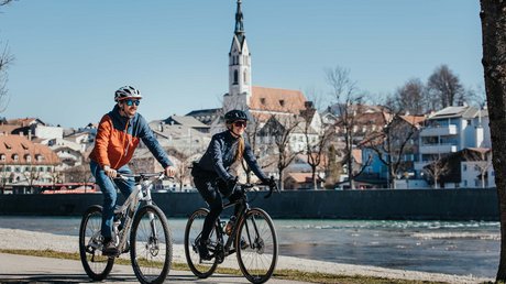 Aussicht auf Traumurlaub in Bad Tölz Zwei Radfahrer fahren an einem Fluss mit Stadt im Hintergrund