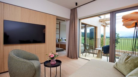 Aussicht auf Traumurlaub in Bad Tölz Gemütliches Wohnzimmer mit Fernseher, Sessel, Tisch, Balkon und Ausblick auf Natur