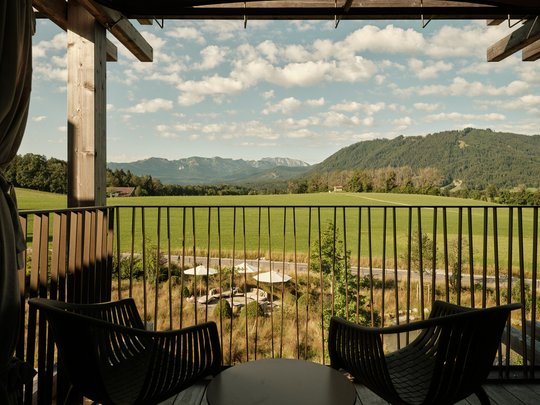 BERGEBLICK: Ihr Hotel in Bad Tölz Balkon mit zwei Stühlen und Tisch mit Blick auf grüne Wiesen und Berge