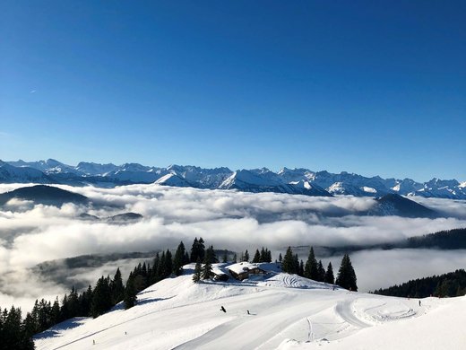 Winter bliss in Bad Tölz Snow-covered mountain with fir trees, chalet and fog below under blue sky