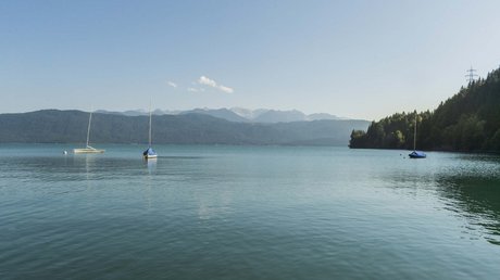 Aussicht auf Traumurlaub in Bad Tölz Drei Segelboote auf ruhigem See vor bewaldeten Bergen und klarem Himmel