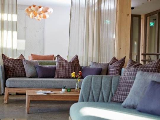 BERGEBLICK: Ihr Hotel in Bad Tölz Modernes Wohnzimmer mit grauen Sofas, gemusterten Kissen und Holztisch mit Blumen