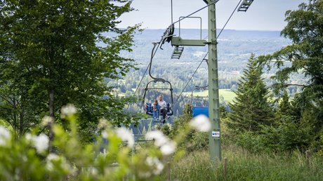 Aussicht auf Traumurlaub in Bad Tölz Mutter und Kind auf Sessellift im grünen Wald mit Bergpanorama