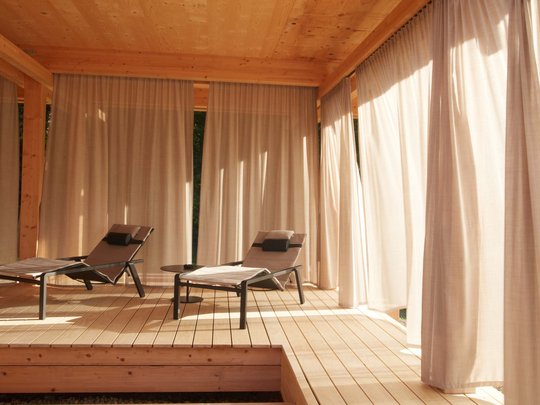 BERGEBLICK: Ihr Hotel in Bad Tölz Zwei Liegestühle auf Holzterrasse mit Vorhängen im warmen Sonnenschein