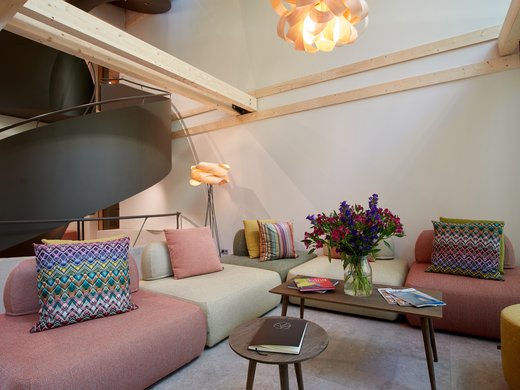 Your lounge for business & indulgence Modern living room with colorful cushions, wooden ceiling beams, and flower vase on table