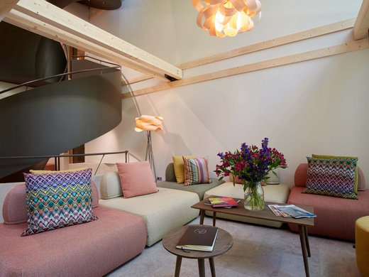 Your lounge for business & indulgence Modern living room with colorful cushions, wooden ceiling beams, and flower vase on table