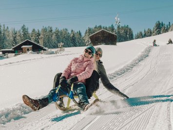 Winter bliss in Bad Tölz Couple sledding together on a snowy slope with cabins in the background