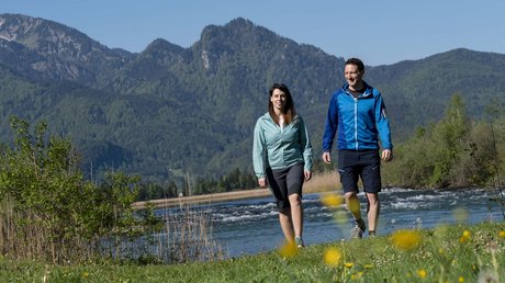 Aussicht auf Traumurlaub in Bad Tölz Paar wandert an einem Fluss mit Bergen und blauem Himmel im Hintergrund