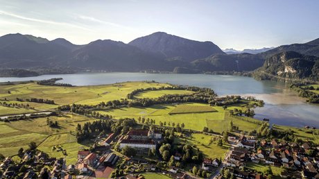 Aussicht auf Traumurlaub in Bad Tölz Luftaufnahme von Wiese, Dorf und See mit Bergen im Hintergrund