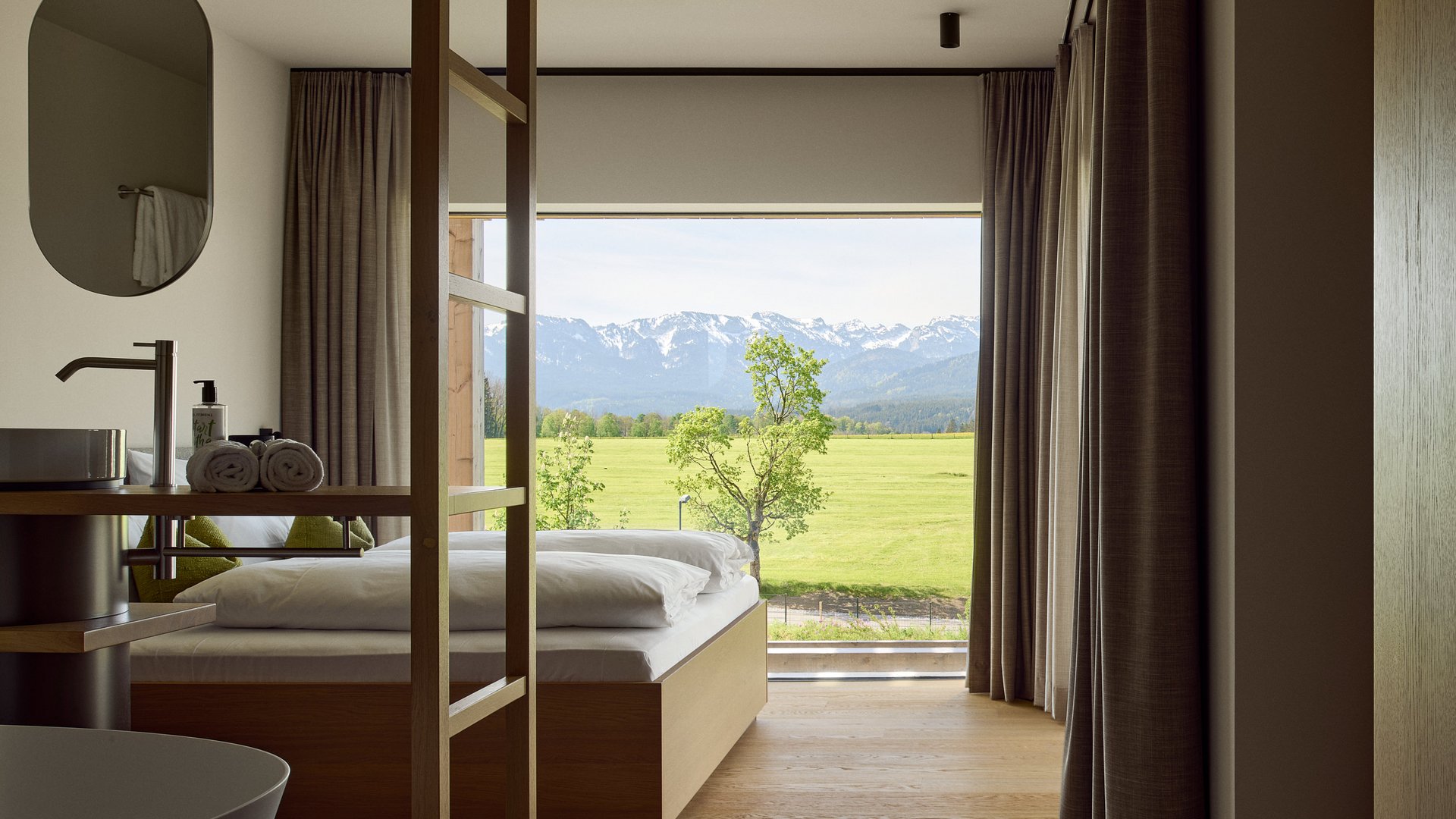 BERGEBLICK: Ihr Hotel in Bad Tölz Modernes Hotelzimmer mit großem Fenster und Blick auf grüne Wiese und Berge