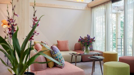 Aussicht auf Traumurlaub in Bad Tölz Gemütliches Wohnzimmer mit bunten Sofas, Blumen und großen Fenstern