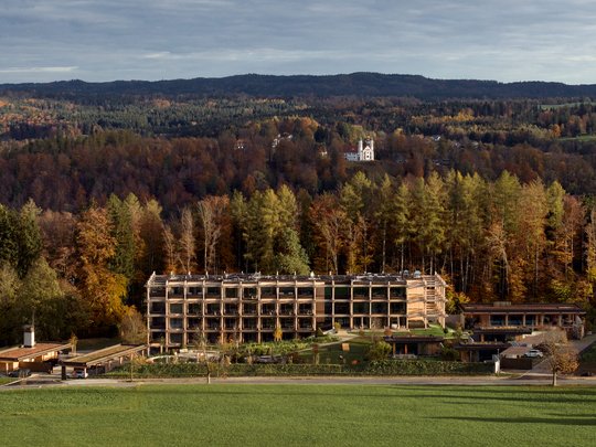 BERGEBLICK: Ihr Hotel in Bad Tölz Modernes Hotel vor herbstlichem Wald und Bergen im Hintergrund