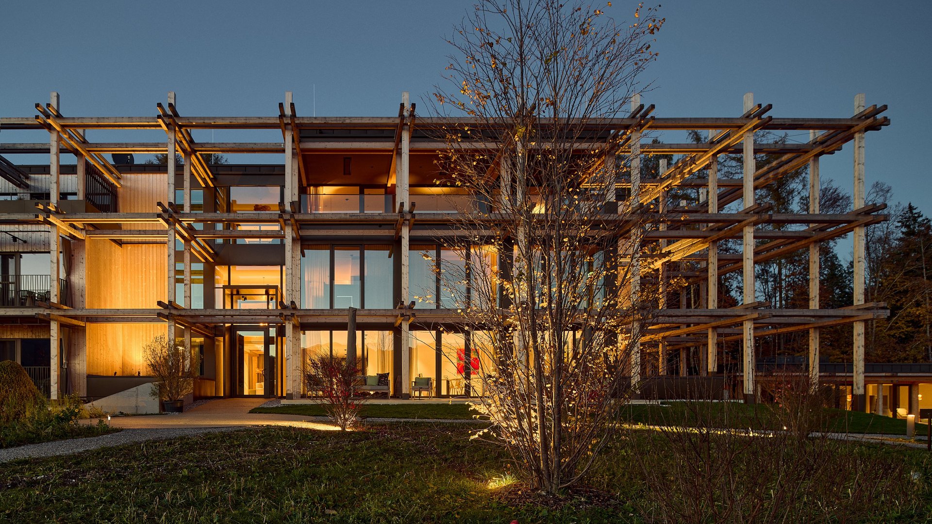 Hotel BERGEBLICK in Bavaria Modern illuminated building with wooden frame and glass facade at dusk