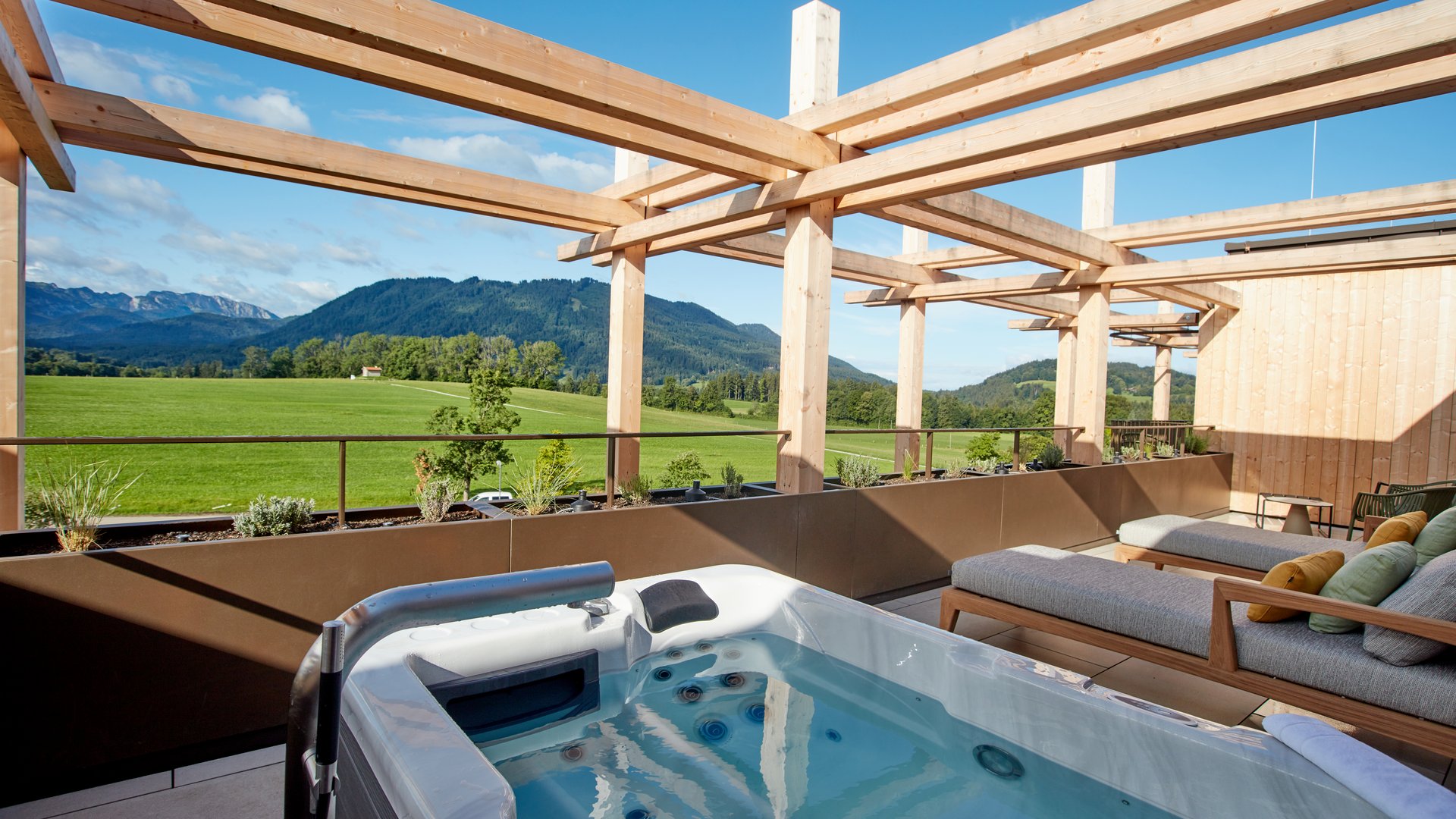 Garden suites in Bavaria: BERGEBLICK Terrace with hot tub and lounge chairs overlooking green fields and mountains