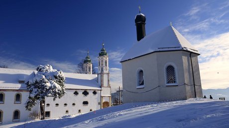 Aussicht auf Traumurlaub in Bad Tölz Schneebedeckte Kirche und Gebäude unter blauem Himmel im Winter