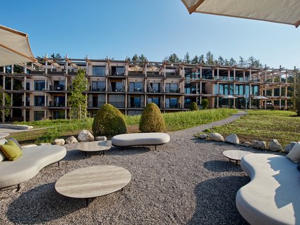 Your holiday in nature in Bavaria: Hotel BERGEBLICK Modern hotel garden with curved sofas and view of wooden building with balconies
