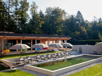 Your holiday in nature in Bavaria: Hotel BERGEBLICK Pool with lounge chairs and umbrellas in front of modern wooden house in garden