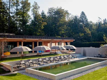 Your holiday in nature in Bavaria: Hotel BERGEBLICK Pool with lounge chairs and umbrellas in front of modern wooden house in garden