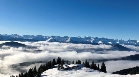 Aussicht auf Traumurlaub in Bad Tölz Schneebedeckte Berge mit Häusern, Bäumen und Wolken unter blauem Himmel