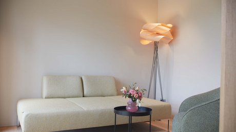 Aussicht auf Traumurlaub in Bad Tölz Minimalistisches Wohnzimmer mit grauem Sofa, Stehlampe und Blumen auf schwarzem Tisch