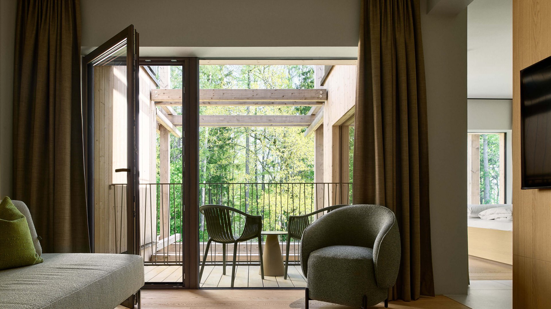 Your holiday in nature in Bavaria: Hotel BERGEBLICK Living room with balcony, green chairs, and view of green trees