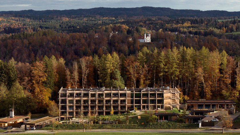 Nachhaltigkeit im BERGEBLICK Modernes Hotelgebäude vor herbstlichem Wald und Hügeln mit Schloss im Hintergrund