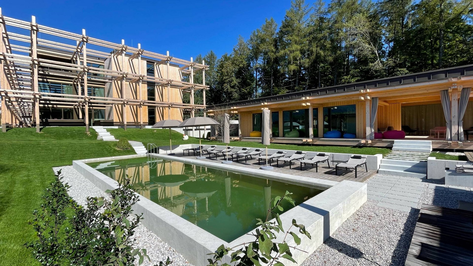 Hotel BERGEBLICK in Bavaria Modern wooden buildings with green lawn and small pond on sunny day