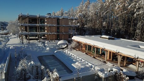 Aussicht auf Traumurlaub in Bad Tölz Verschneites modernes Gebäude mit Pool und Wald im Hintergrund unter klarem blauen Himmel