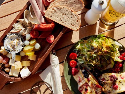 Bad Tölz: hotel with regional breakfast Platter with meats, cheese, bread, salad, and a glass of beer on wooden table