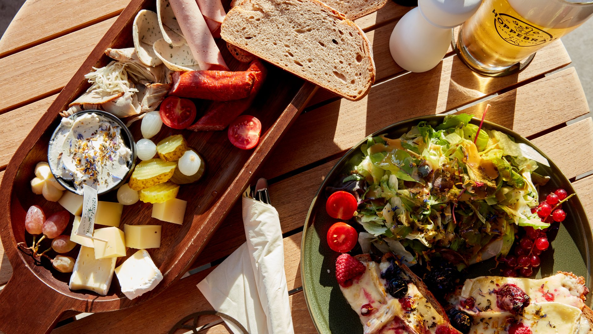 Your lounge for business & indulgence Platter with meats, cheese, bread, salad, and a glass of beer on wooden table