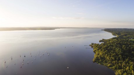 Aussicht auf Traumurlaub in Bad Tölz Luftaufnahme eines Sees mit Segelbooten und bewaldetem Ufer bei Sonnenlicht