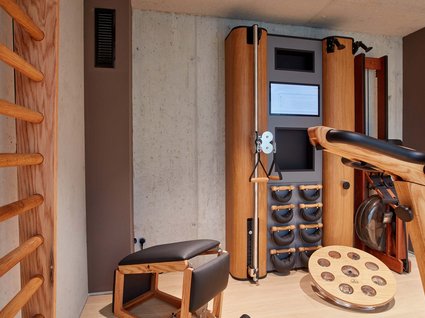 Dein Aktivurlaub im Hotel mit Fitnessstudio in Bayern Moderner Fitnessraum mit Holztrainingsgeräten und Rudergerät an Betonwand