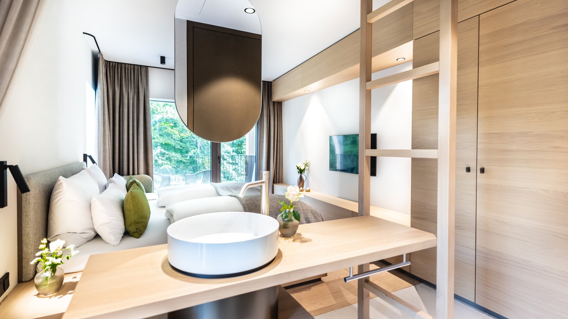 Sonja Sindlhauser Modern hotel room with wooden accents, sink, and double bed with green pillows