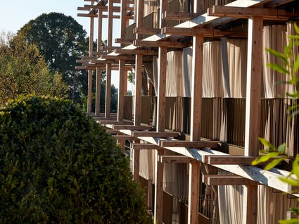 Your holiday in nature in Bavaria: Hotel BERGEBLICK Facade with wooden frames and curtains beside green bushes and trees