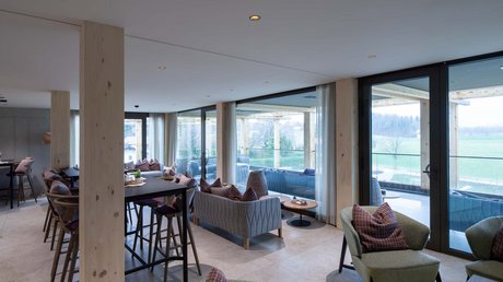 Aussicht auf Traumurlaub in Bad Tölz Moderner Wohnraum mit Sofas, Tischen und großen Fenstern mit Blick auf die Landschaft