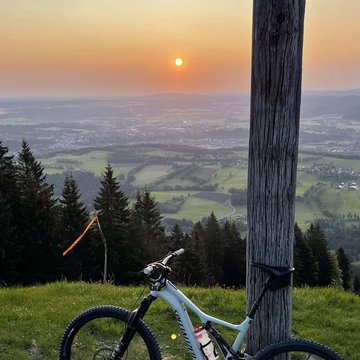 BERGEBLICK: Ihr Hotel in Bad Tölz Mountainbike lehnt an einem Holzmast mit Blick auf Sonnenuntergang und Tal