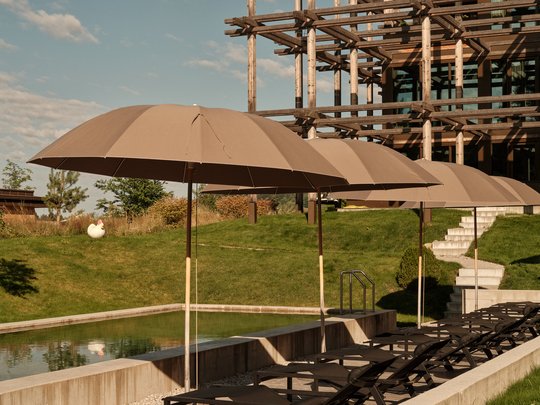 BERGEBLICK: Ihr Hotel in Bad Tölz Reihe brauner Sonnenschirme über Liegestühlen neben Pool mit Holzgebäude im Hintergrund